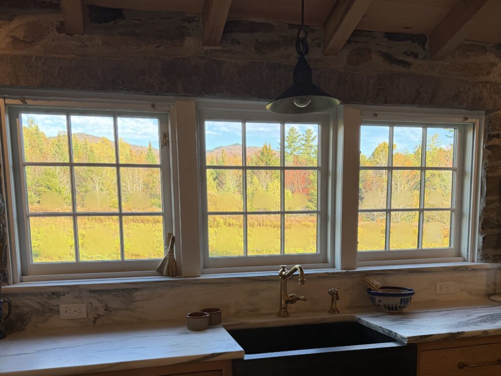 Kitchen window overlooking a vibrant autumn landscape with colorful trees and mountains in the distance.
